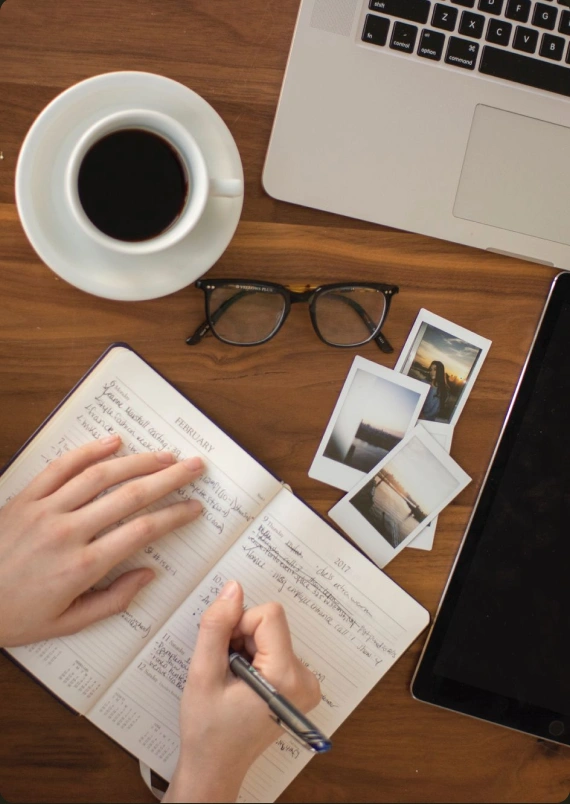 Writer working in a notebook beside coffee and a laptop